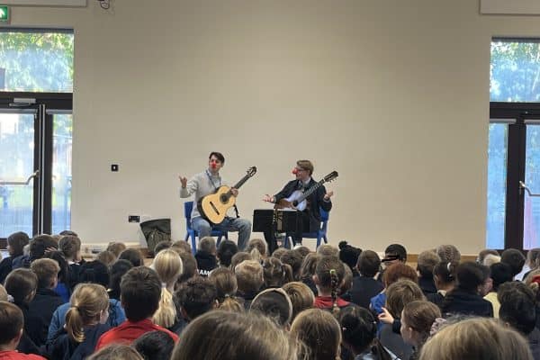 Two male musicians performing the guitar to school children